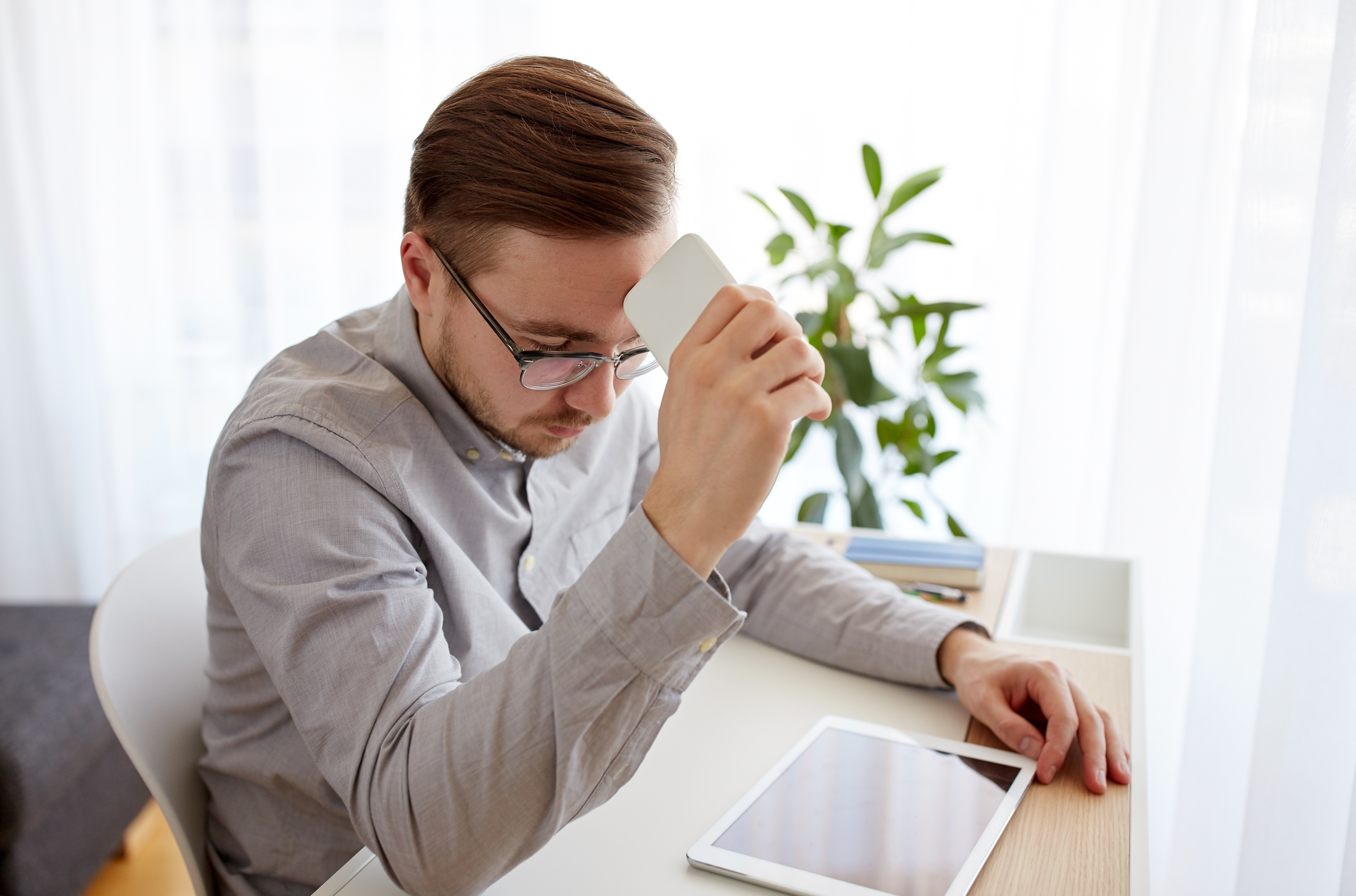 Businessman holds smartphone to his forehead while closing his eyes in a moment of fear. [How to Face Your Fears About Cold Calling a Donor]