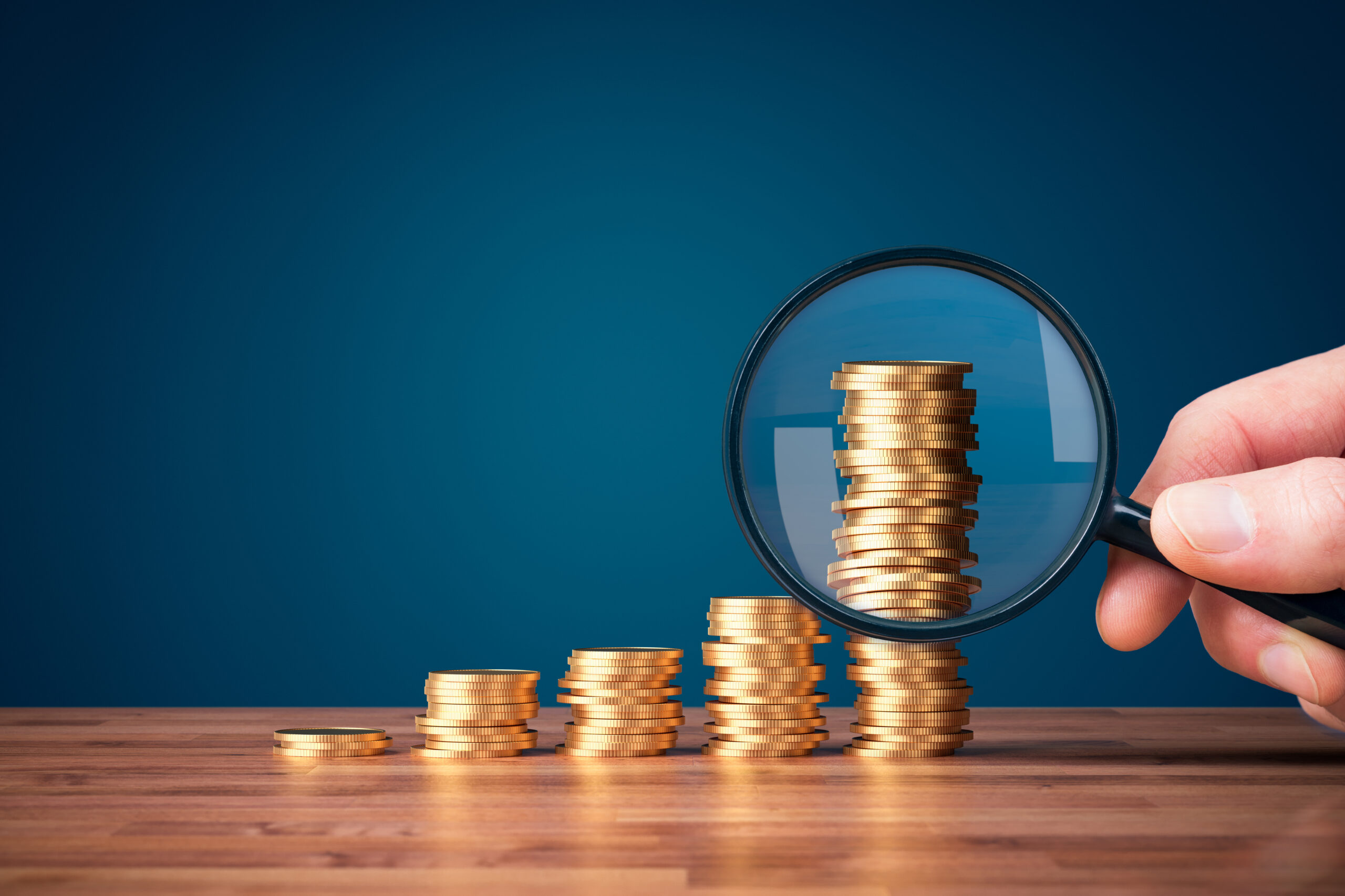 A magnifying glass examining stacks of coins [Stop Using Donor Wealth Ratings to Build a Portfolio]