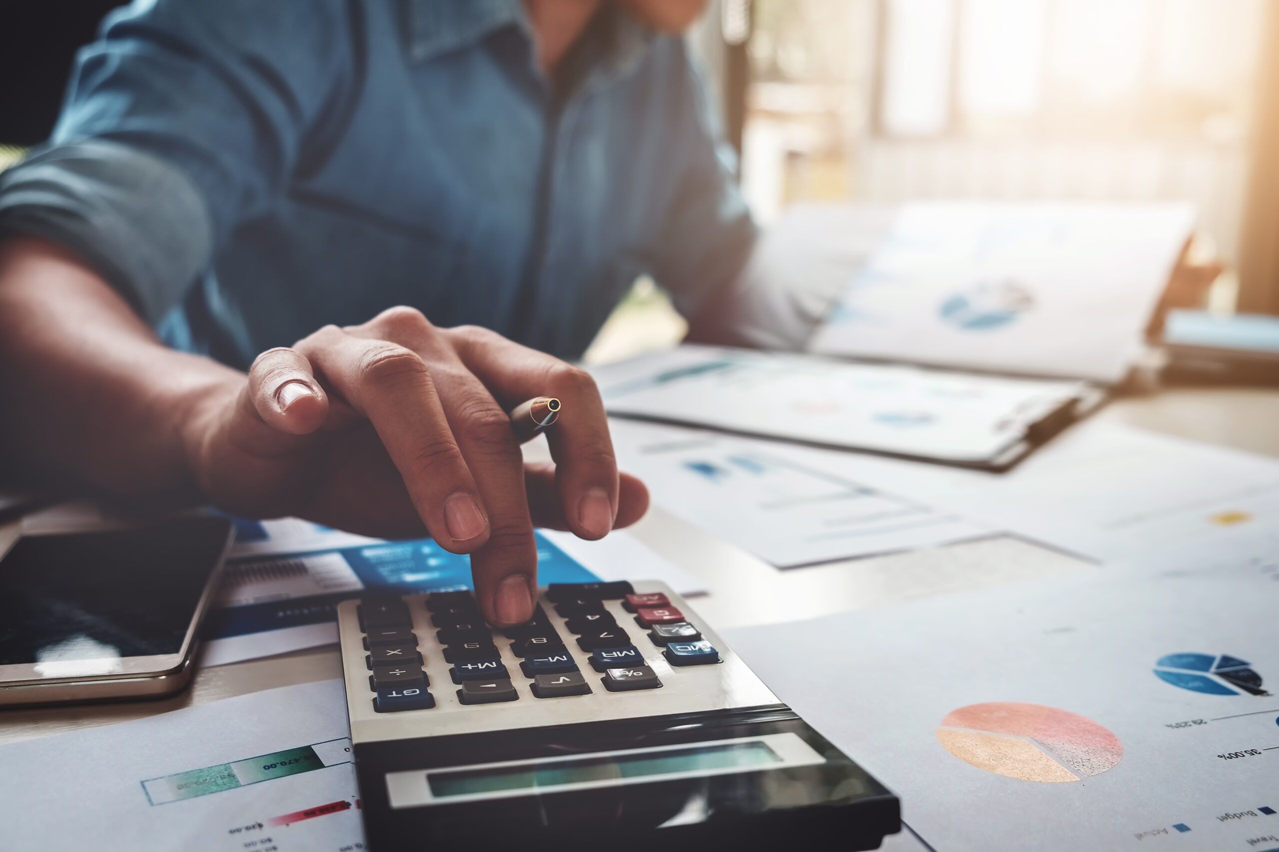 A closeup of a person doing their fundraising budget calculations at a table with graphs and a calculator.